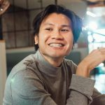 Close-up of a smiling Asian man wearing a sweater indoors.